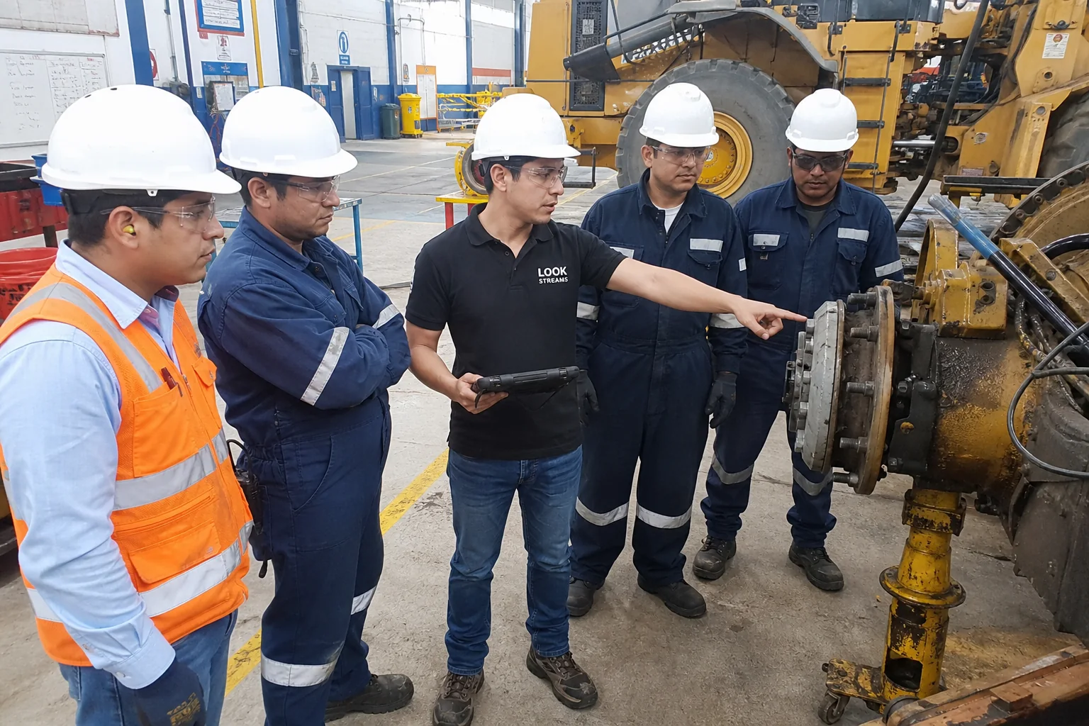 Líder técnico joven de Look Streams explica una inspección a ingenieros junto a maquinaria pesada.